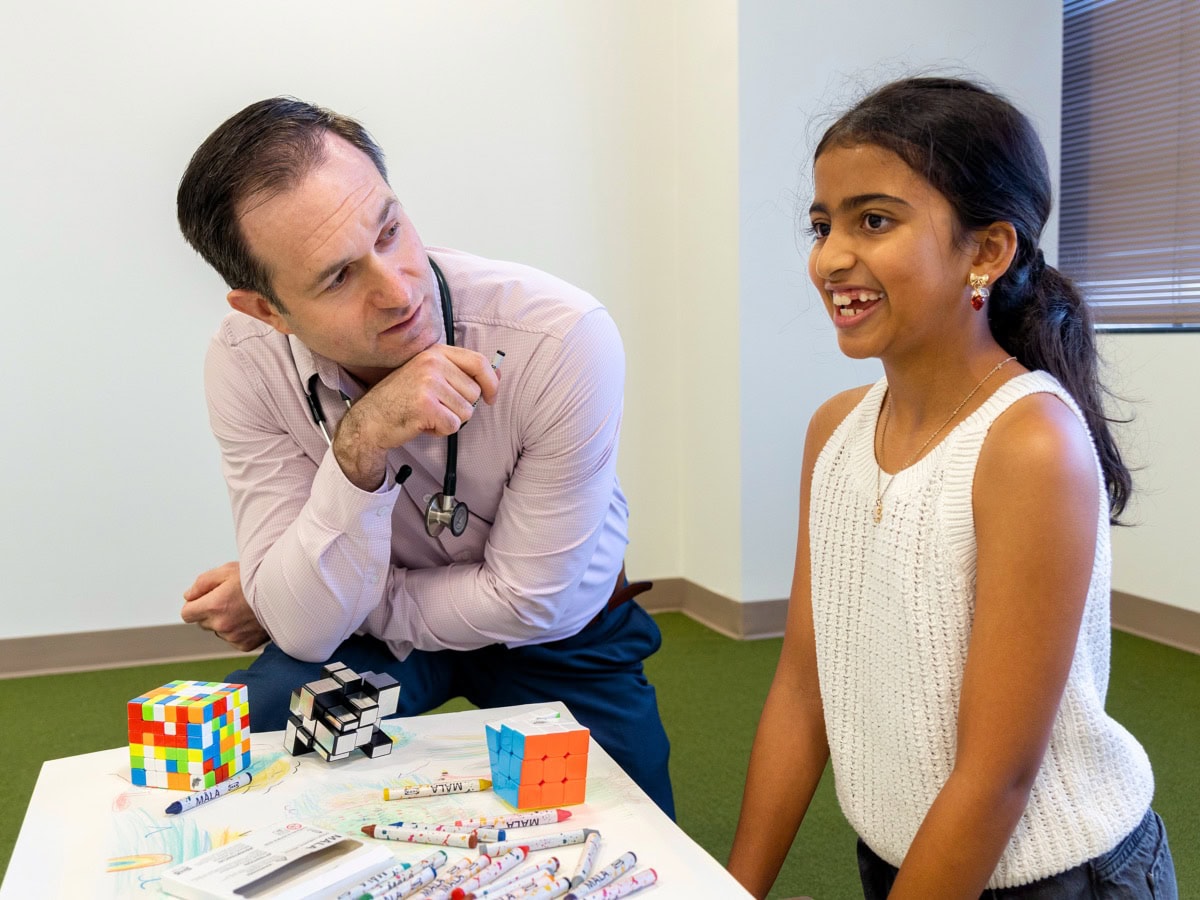 dr daniel gossett works thoughtfully with a patient in his clinic. Sitting at a table with some toys and games.